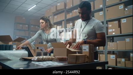 Multiethnische Lagerbeamte, Postarbeiter, die Kartons mit Online-Bestellungen verpacken, Pakete für den Versand an Kunden vorbereiten. Modernes Sortierzentrum des E-Commerce-Stores, Lieferservice. Stockfoto