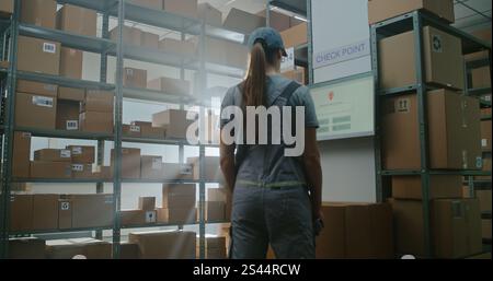 High-Tech Advanced Sorting Center: Lagerarbeiter im futuristischen Ganzkörper-Roboter-Exoskelett geht mit schwerer Kartonbox. Logistikspezialistin Scannt Paket Und Überprüft Versandinformationen. Stockfoto