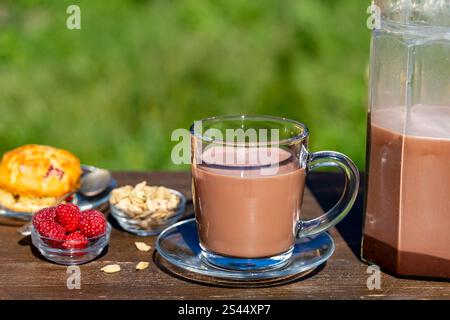 Indischer Masala Chai oder Tee oder Kakao im Glas mit Kanne und Himbeermuffin auf dem Holztisch im Café auf Naturhintergrund, Nahaufnahme. Trendig gesund d Stockfoto
