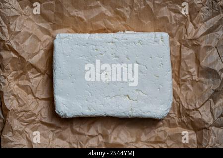 Stück frischer weißer Hüttenkäse auf Lebensmittelpapier, Nahaufnahme, Draufsicht. Hausgemachter Weißkäse aus Kuhmilch auf Papierhintergrund Stockfoto