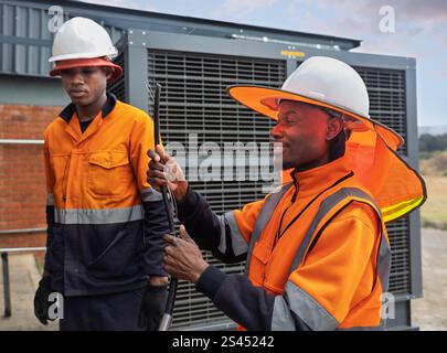 afroamerikanische Arbeiter Kollegen, reparieren hlk-Einheit, mit orangefarbener Schutzausrüstung, Schutzhelm, Sonnenschutzhut für Sonne mit Nackenklappe Stockfoto