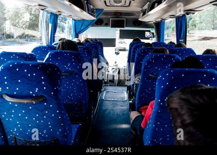 Menschen sitzen auf blauen Stühlen in einem großen Stadtbus, vor dem Fenster eine Stadtlandschaft an einem sonnigen Sommertag Stockfoto