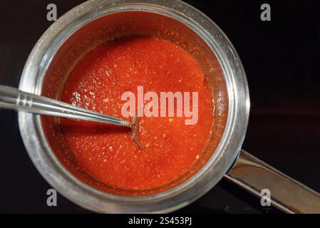 Tomatensauce mit Löffel in der Pfanne. Rote Soße in der Küche machen. Draufsicht Stockfoto