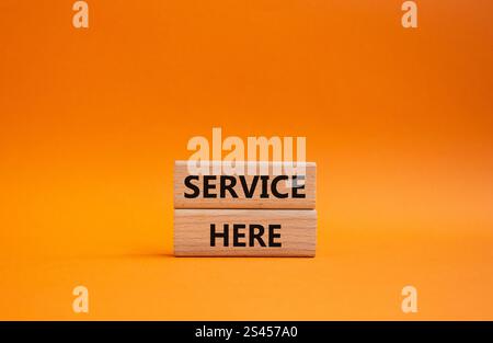 Symbol „Service here“. Concept Words Service hier auf Holzblöcken. Wunderschöner orangefarbener Hintergrund. Business and Service Here Konzept. Kopierbereich. Stockfoto