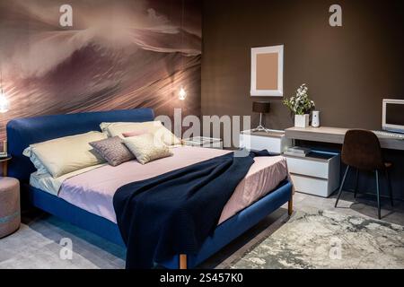 Komfortable und moderne Schlafzimmereinrichtung mit blauem Bett und funktionellem Arbeitsbereich Stockfoto