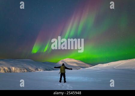 Ein Mann, der unter erstaunlicher Darstellung der Aurora Borealis, auch bekannt als Nordlichter, im arktischen Tromso, Norwegen steht. Wundervolle Lichtshow in verschneiten Bergen. Stockfoto