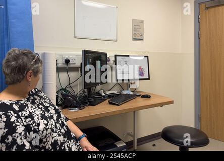 Ältere Frau mittleren Alters in GP Ärzte Chirurgie Termin, die Informationen, die vom Arzt auf dem Bildschirm zur Verfügung gestellt werden - Herz Zustand Diagramm Krankenhaus Stockfoto