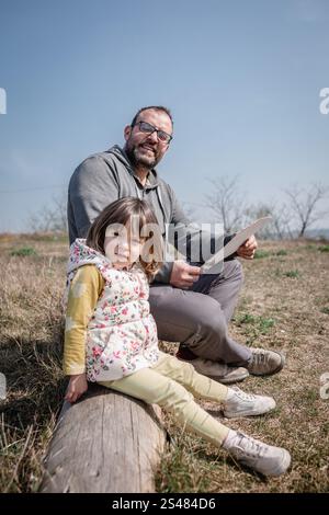 Tiefwinkelansicht des Vaters, der mit Tochter auf dem gefallenen Baumstamm sitzt Stockfoto