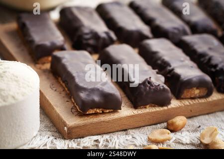 Hausgemachte gesunde Riegel aus Molkenproteinpulver und Erdnussbutter, umhüllt mit dunkler Schokolade Stockfoto