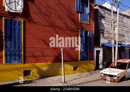 Pulsierende Straßenszene in La Boca, Buenos Aires, Argentinien, mit farbenfrohen Gebäuden und einem verlassenen Auto. Stockfoto