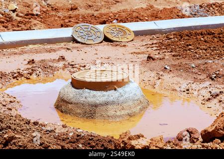 Entwässerungsschacht steht in matschigem Boden, Wasser, umgeben von Baustelle Stockfoto