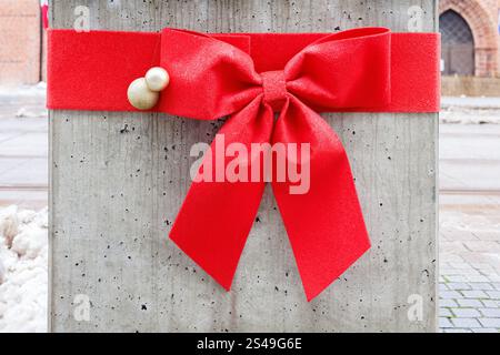 Dekoration in Form einer großen roten Schleife mit Weihnachtskugeln um eine Betonsäule. Stockfoto