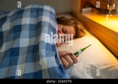 Frau liegend im Bett mit Grippesymptomen und einem Thermometer in der Hand Stockfoto