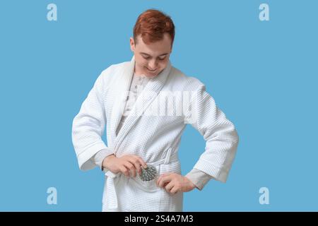 Junger Mann mit Haarkopfmassagegerät auf blauem Hintergrund Stockfoto