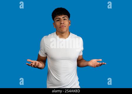 Porträt eines verwirrten, ahnungslosen jungen lateinischen Mannes, der mit den Schultern zuckt, Gesten macht, die ich nicht weiß, haben keine Ahnung vor blauem Hintergrund Stockfoto