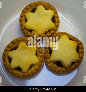 Drei traditionelle Hackkuchen mit sternförmigen Spitzen auf einer weißen Platte, perfekt für Festlichkeiten und Feiertage. Stockfoto