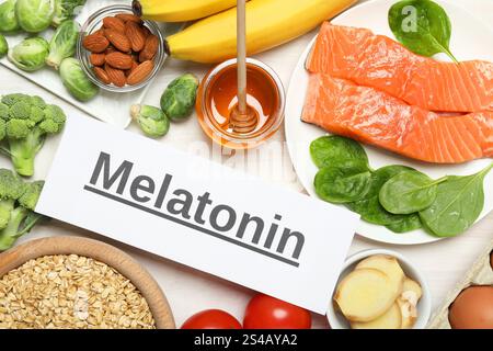 Wort Melatonin und verschiedene Produkte auf weißem Holztisch, flach gelegt Stockfoto
