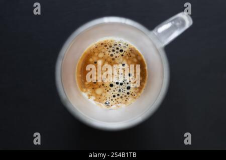 Blick von oben auf einen frisch gebrühten Espresso in einer Glasschale mit schaumiger Crema und Blasen auf dunklem Hintergrund. Stockfoto