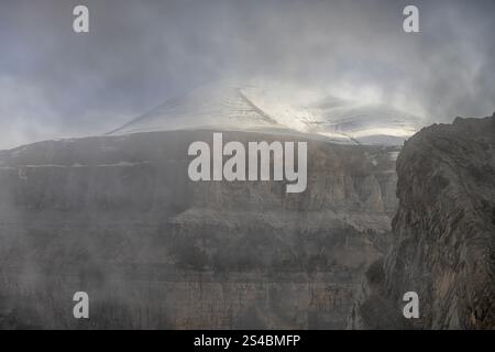 Hoch aufragende Klippen mit Blick auf einen dichten Wald und schneebedeckte Gipfel schaffen einen atemberaubenden Kontrast aus Texturen und Farben. Stockfoto