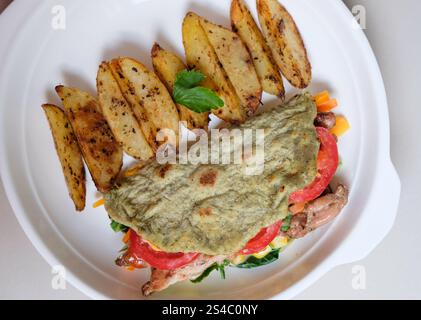 Gebackene Kartoffelscheiben und Tortilla-Wrap mit gebratenem Huhn und Vegeteble, serviert auf einem Teller. Stockfoto