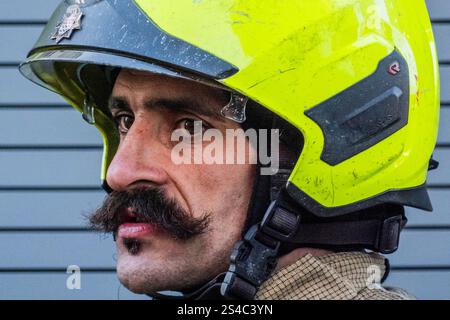 London, Großbritannien. Januar 2025. Ein Feuerwehrmann mit einem kräftigen Schnurrbart beobachtet den Fortschritt - das eisige Wetter lässt eine kleine Menge Mauerwerk von der Spitze eines der vierstöckigen Gebäude auf die Straße fallen. Zahlreiche Polizeibeamte und zwei Feuerwehrfahrzeuge nahmen an dem Unfall im Zentrum von Hampstead Teil. Guy Bell/Alamy Live News Stockfoto