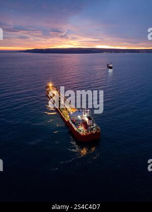Aus der Vogelperspektive eines hell beleuchteten Tankschiffes auf dem Meer während der Dämmerung, umgeben von offenem Wasser und einem leuchtenden Horizont Stockfoto