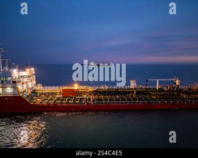 Aus der Vogelperspektive eines hell beleuchteten Tankschiffes auf dem Meer während der Dämmerung, umgeben von offenem Wasser und einem leuchtenden Horizont Stockfoto
