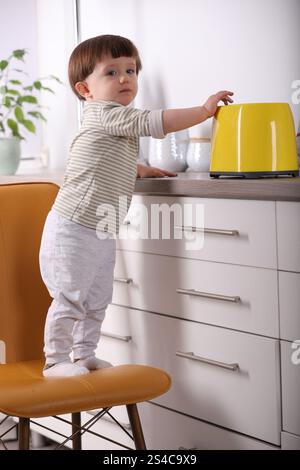 Kleiner Junge, der mit Toaster in der Küche spielt. Gefährliche Situation Stockfoto