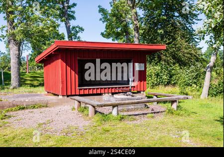 Eine Holzwindschutzhütte, die rot lackiert ist, mit einem Kamin vor der Öffnung, die als schützende Ruhestelle für kurzfristige Nutzung gedacht ist. Stockfoto