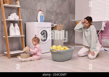 Müde Hausfrau mit ihrer kleinen Tochter, die sich ausgeruht hat, nachdem sie zu Hause gewaschen hat Stockfoto