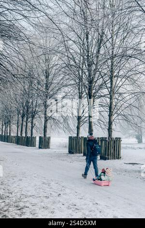 Ein Mann zieht seine Kinder auf einem Schlitten durch den Winterschnee in Großbritannien. Vereiste Bedingungen und tückische Fahrbedingungen wie der alte Schnapper beißt. Stockfoto