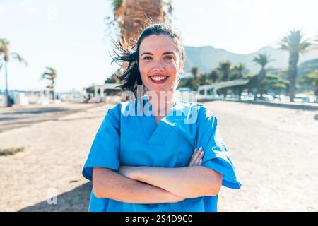 Eine Ärztin in einem blauen Hemd steht lächelnd am Strand. Stockfoto