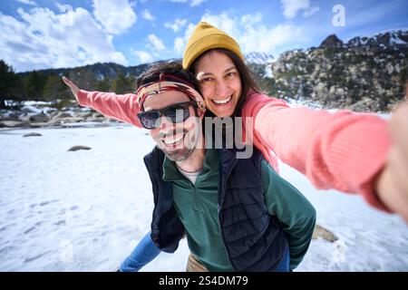 Fröhliche multirassische nette junge Paare posieren Huckepack für mobiles Foto am Wintertag draußen. Stockfoto