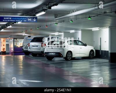 Straßburg, Frankreich - 11. Januar 2025: Eine Tiefgarage am Gare de Strasbourg mit geparkten Fahrzeugen, beleuchteten Ausstiegsschildern und di Stockfoto