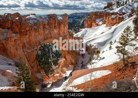 Natural Bridge im Bryce Canyon National Park, Süd-Utah, USA, mit Schnee auf dem Boden und einigen grauen Wolken am Himmel. Stockfoto