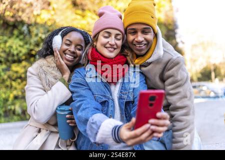 Multirassische junge Freunde, die Spaß haben, gemeinsam ein Selfie mit Smartphone in einer winterlichen Stadt zu machen Stockfoto