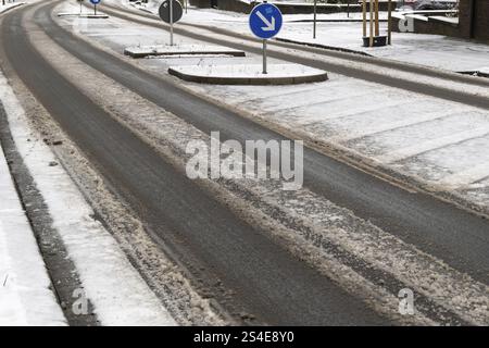 Schmelzender Schnee erzeugt während der Wintersaison Spuren auf einer teilweise freigelegten Asphaltstraße, wobei ein Schild „Keep Left“ (links halten) den Verkehrsfluss anzeigt Stockfoto