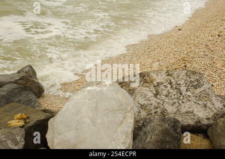 Close Up Diagonal Blick auf große Felsen am St. Pete Beach, Florida mit Sand und schaumigem Wasser. Weiße Kappenwellen spritzen auf und über große Felsen Stockfoto