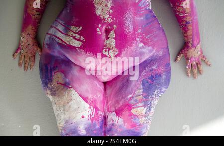 Die lebendige Nahaufnahme zeigt eine große Karosserie mit kräftigen Pink-, Lila- und Goldspritzern, die Kunst und Form miteinander verbindet. Ausdrucksstarke Hände ruhen auf einem Neutr Stockfoto