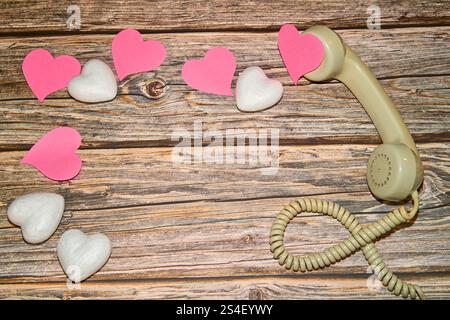 Altes Kabel-Headset mit einem Haufen rosa und weißer Herzen auf einem Holztisch Stockfoto