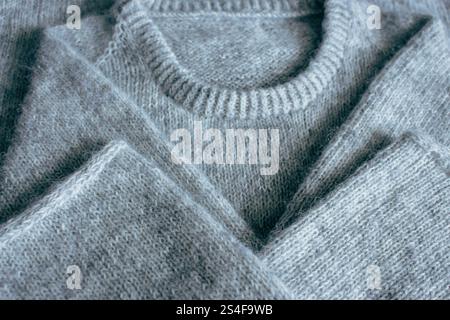 Grau melierter Strickpullover mit abnehmbarer i-Kordelbindung. Mischung aus grauer Wolle und weißem Kaschmir. Hintergrund des Strickmusters. Strick Lifestyle. Gemütliches Hobby. Stockfoto