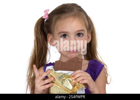 Ein vierjähriges Mädchen isst Schokolade und macht eine Geste. Fotografiert auf weißem Hintergrund Stockfoto