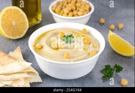 Klassischer Kichererbsenhummus mit Pita, Olivenöl, Petersilie und Zitrone auf grauem Hintergrund. Arabische und türkische Küche. Stockfoto