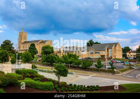 Eine Kirche mit einem großen Kirchturm steht im Hintergrund eines bewölkten Tages. Die Kirche ist von Bäumen und Gebäuden umgeben Stockfoto