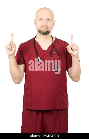 Ein glatzköpfiger Arzt mit Bart, mit roten Schutten und einem Stethoskop um den Hals, zeigt mit beiden Zeigefingern nach oben. Stockfoto
