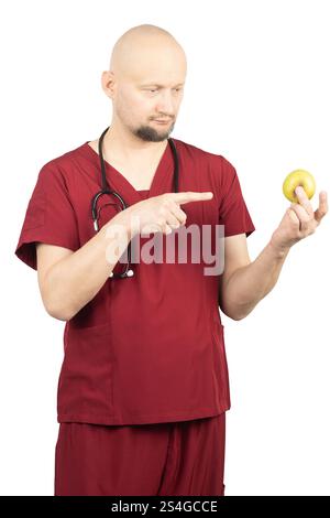Ein glatzköpfiger Arzt mit Bart, mit roten Peelings und einem Stethoskop um den Hals, hält einen grünen Apfel Stockfoto