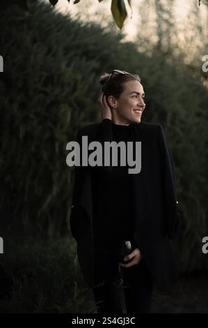 Mädchen mit einem Glas Weinrebe auf einer Party im Garten in schwarzem Anzug Stockfoto