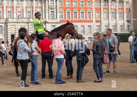 LONDON, GROSSBRITANNIEN - 19. SEPTEMBER 2014: Nicht identifizierte Touristen hören sich Anweisungen von einem berittenen Polizisten an, bevor eine berittene Wache entlarvt wird Stockfoto