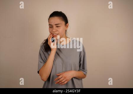 Die Frau fängt ihr Zahnfleisch mit einem schmerzhaften Ausdruck an und fängt das Gefühl von Zahnschmerzen ein. Ihre Körpersprache spiegelt körperliche Unannehmlichkeiten wider. Die Stockfoto