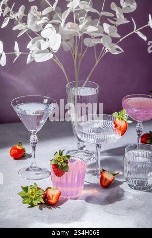 Erfrischende Erdbeercocktails in Kristallglas, garniert mit frischen Erdbeeren und dekorativen weißen Blättern, schaffen eine elegante Szene Stockfoto